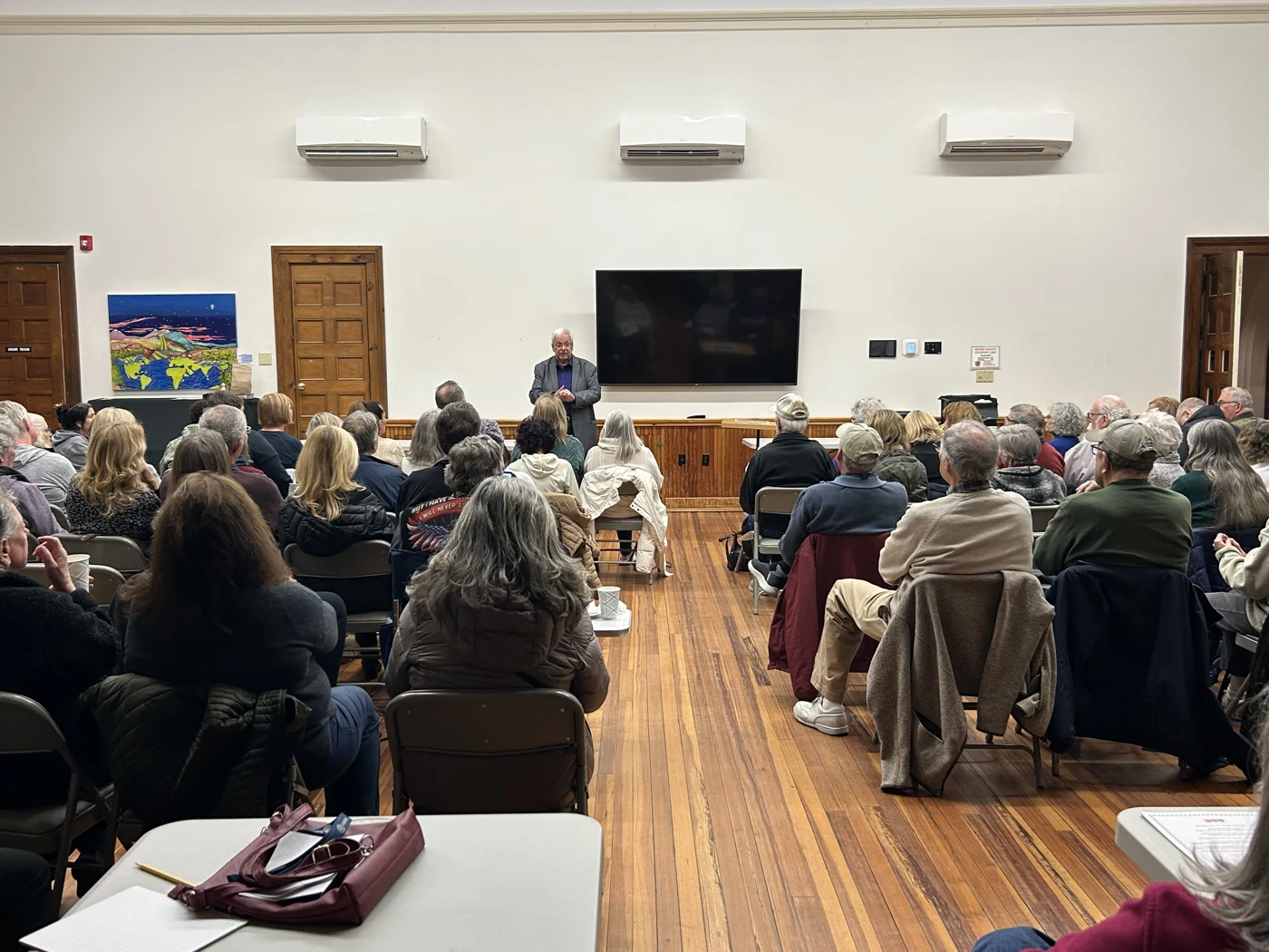 A seated audience watching Jim Sisti perform at the front of a room